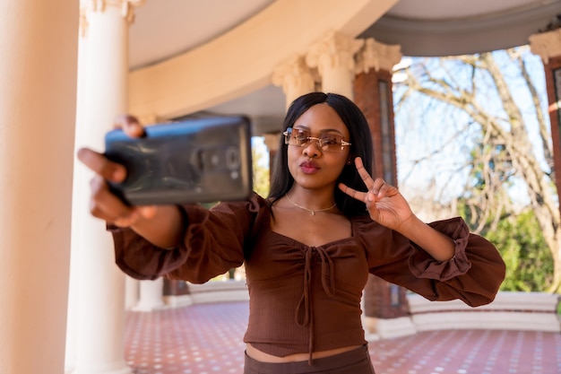 A beautiful natural young African woman in a park With sunglasses taking a selfie lifestyle