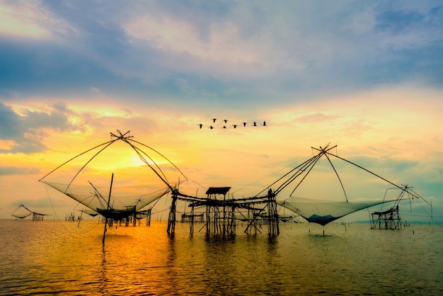 Beautiful nature landscape golden light of the morning sky at sunrise with flock of birds are flying over the native fishing tool, rural lifestyle at Pakpra canal, Baan Pak Pra, Phatthalung, Thailand