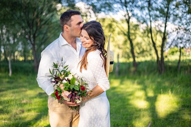 Beautiful newlyweds stand on a green meadow and kiss rustic style wedding