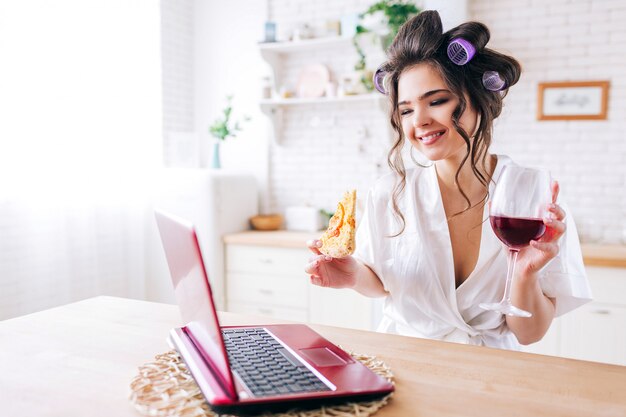 Beautiful nice young woman look on laptop and smile. Stand in kitchen. Housekeeper watching movie. Alone in room. Leisure activity. Careless lifestyle without work.