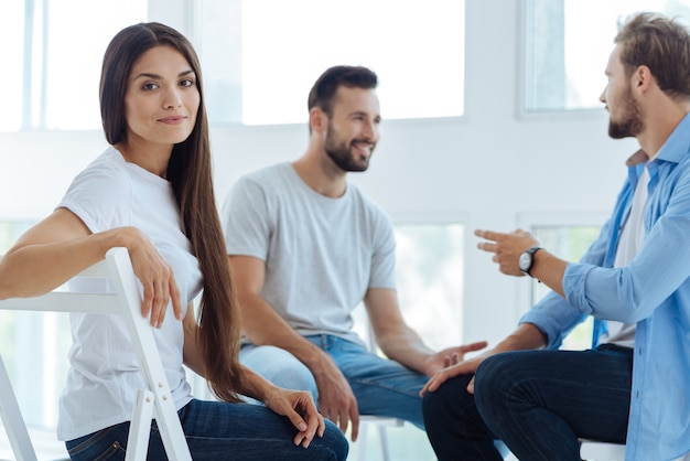 Beautiful nice young woman sitting on the chair and looking at you while visiting a psychological session