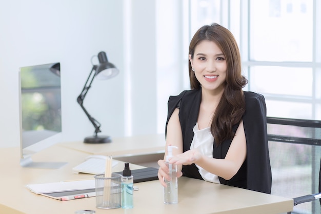 A beautiful office lady is sitting and pressing an alcohol gel to happily wash hands at work