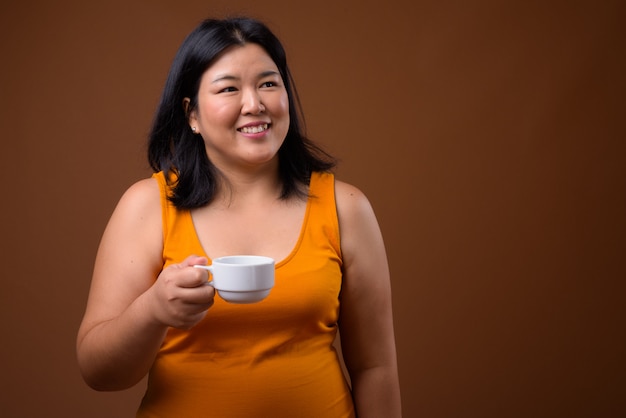 beautiful overweight Asian woman wearing orange sleeveless dress on brown