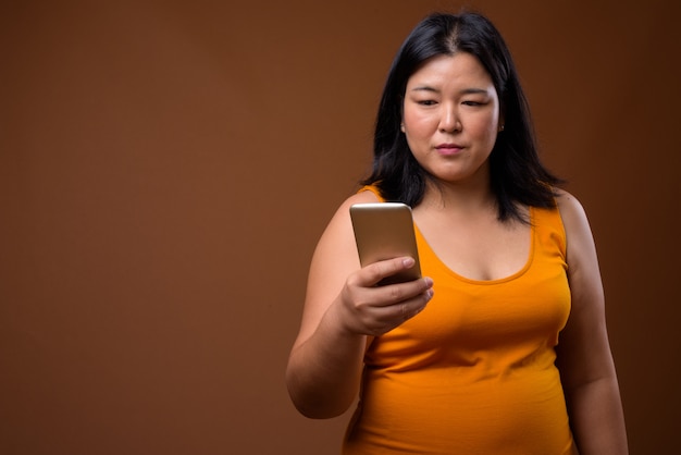 beautiful overweight Asian woman wearing orange sleeveless dress on brown