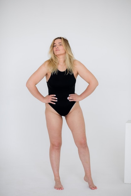 Beautiful overweight woman in black swimsuit on white wall