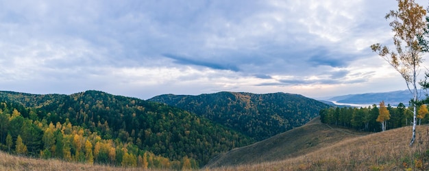 Beautiful panoramic view of the hills and the river against the background of dark clouds with the setting sun