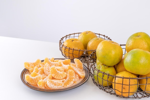 Beautiful peeled tangerines in a plate and metal basket isolated on bright white clean table in a modern contemporary kitchen island close up