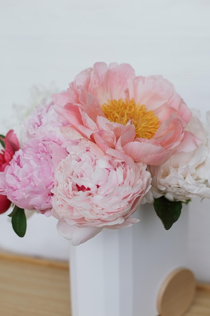 Beautiful peonies bouquet in modern stylish vase on white wooden background copy space Mothers day