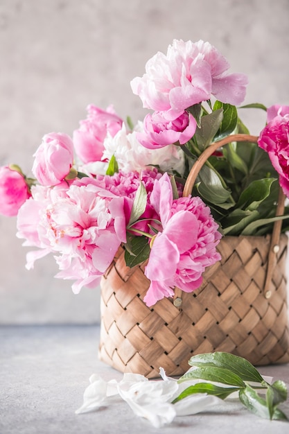 Beautiful peonies in wicker basket on wooden table