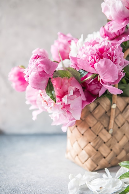 Beautiful peonies in wicker basket on wooden table