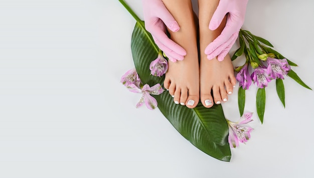 Beautiful perfect female feet top view with tropical flowers and green palm leaf