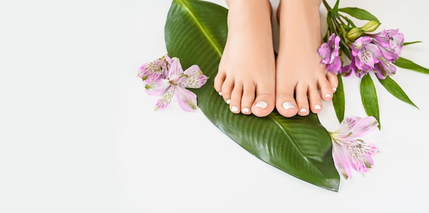 Beautiful perfect female skin legs feet top view with tropical flowers and green palm leaf