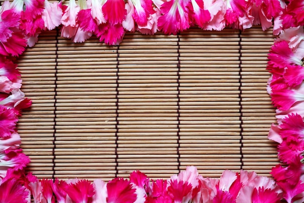 Beautiful pink carnations petals flowers frame on bamboo mat background. Valentine's day.