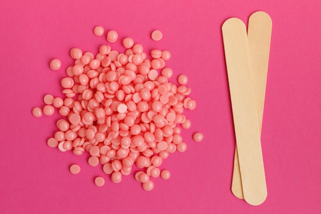 Beautiful pink depilatory wax granules and wooden spatulas on magenta background Epilation