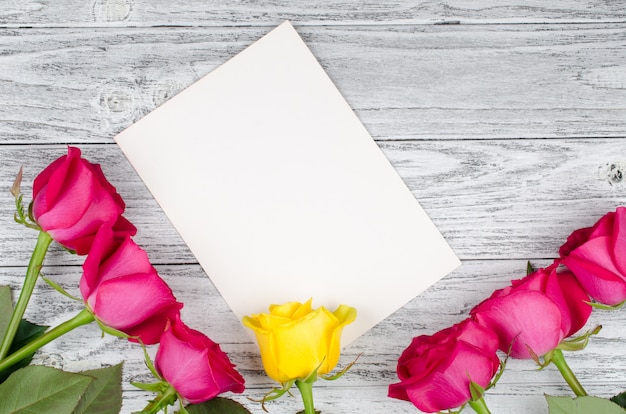 Beautiful pink roses and a single yellow rose on a blank white greeting card against a worn wooden background