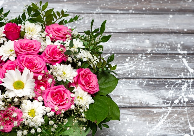 Beautiful pink roses and white daisies in a box on a gray wooden background.