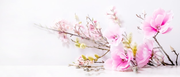 Beautiful pink spring flowers composition over white. Magnolia flowers, cherry blooming branches and willow.