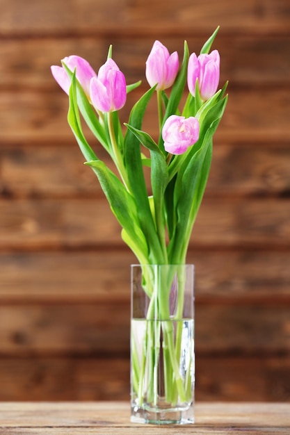 Beautiful pink tulips in vase on table on wooden background