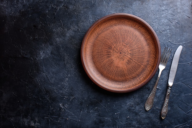 A beautiful plate for food, a dish, browns, a fork, a knife, against a dark background.