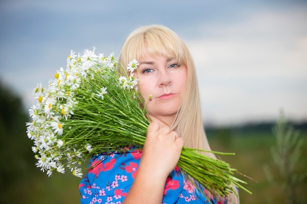 A beautiful plus size girl with white hair in a summer dress poses on the street with daisies