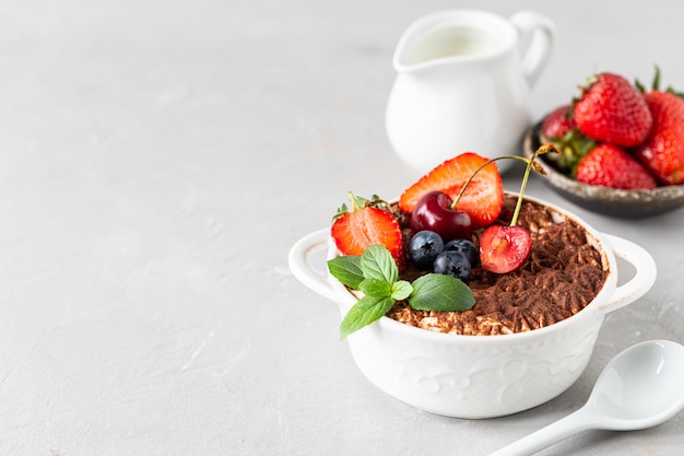 A beautiful portioned serving of Italian tiramisu dessert, garnished with strawberries, cherries and mint on a white background. Copy space for your text.