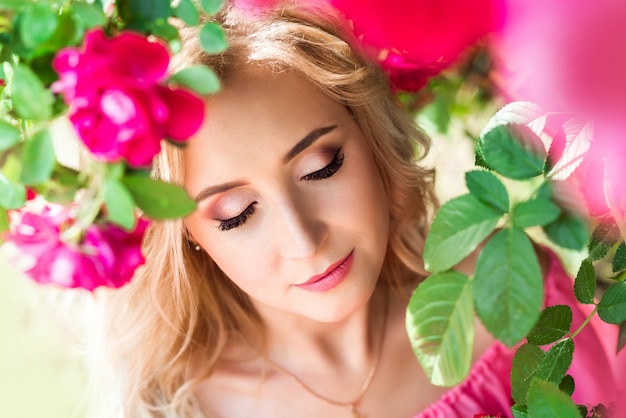 Beautiful portrait of a blonde woman in pink roses. close-up, makeup, extended eyelashes