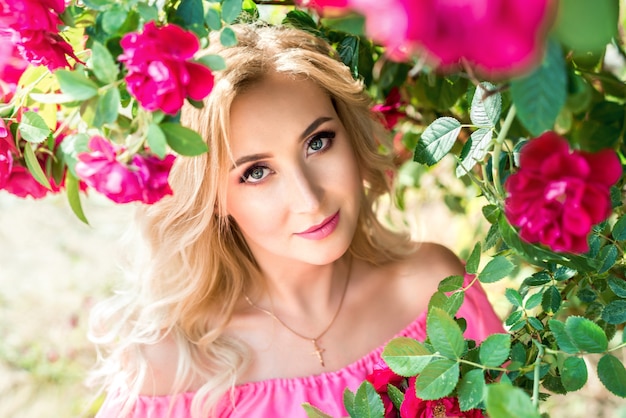 Beautiful portrait of a blonde woman in pink roses. close-up, makeup, extended eyelashes