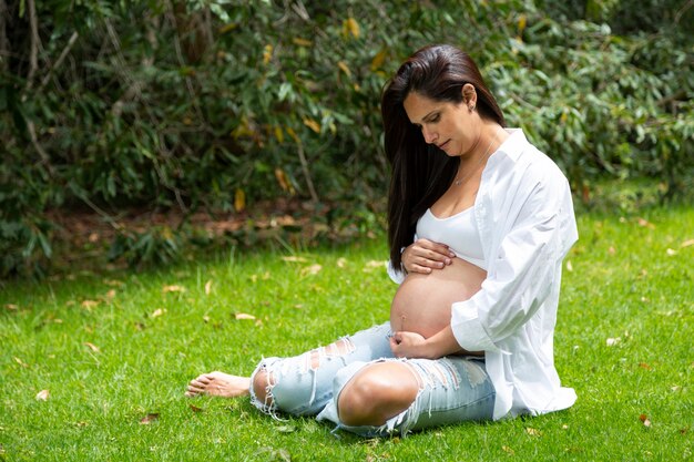 Beautiful portrait of pregnant woman sitting on the grass in a natural park. 