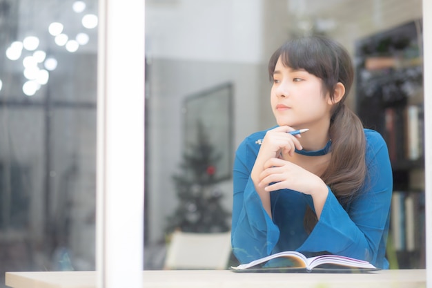 Beautiful portrait young asian woman writer smiling thinking idea and writing on notebook