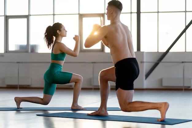 Beautiful positive couple working out in gym doing health exercises doing lunges on the mat