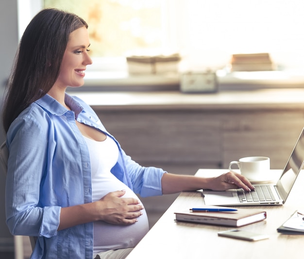 Beautiful pregnant business woman is using a laptop.