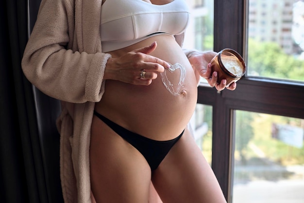 Beautiful pregnant woman in bathrobe applies a cream to her bell