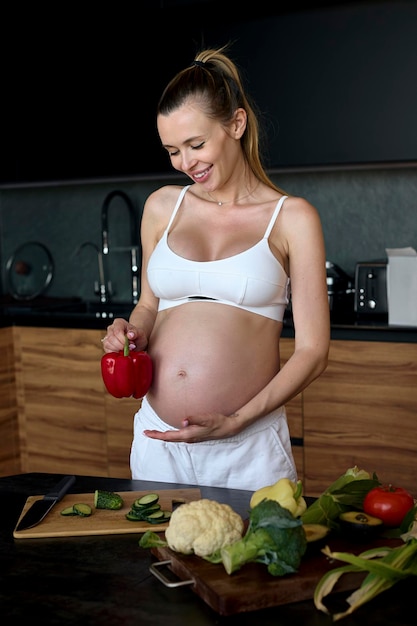 Beautiful pregnant woman making fruits smoothies with blender H