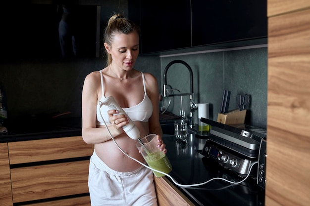 Beautiful pregnant woman making fruits smoothies with blender H