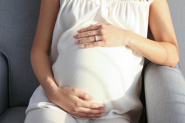 Beautiful pregnant woman sitting in armchair at home closeup