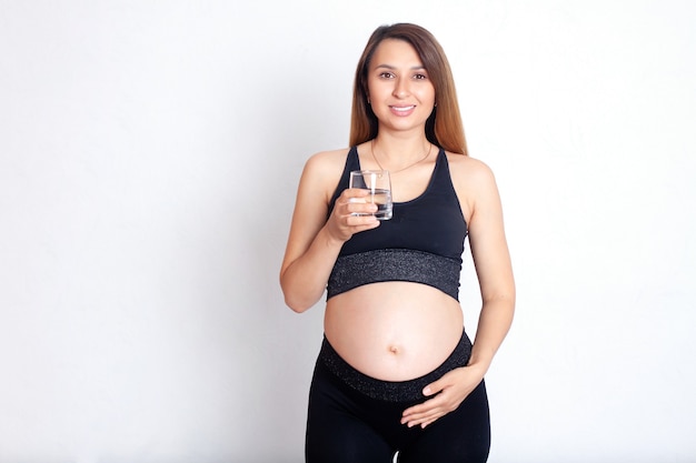 A beautiful pregnant woman in a sports uniform holds a glass of clean water in her hand