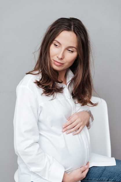 Beautiful pregnant woman in studio looking away gray background