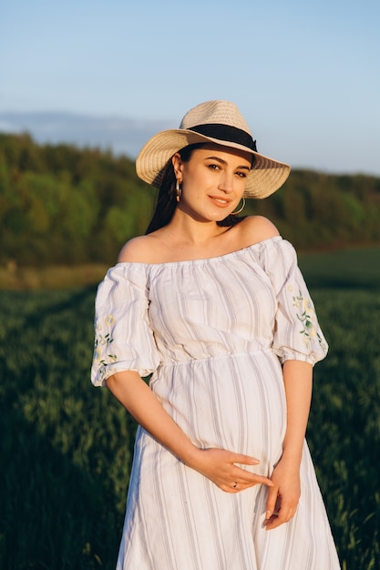 Beautiful pregnant woman in the summer nature meadow in sunset