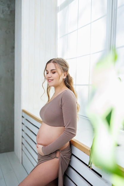 A beautiful pregnant woman in a top and skirt hugs her belly Stylish pregnant woman