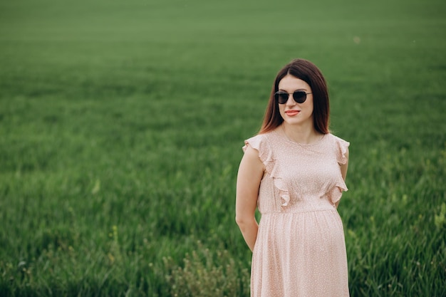 Beautiful pregnant woman wearing a dress and hat in a green field with flowers