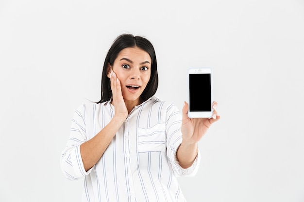 beautiful pregnant woman with big belly smiling and holding smartphone in hand while standing isolated over white wall