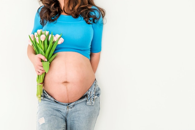 A beautiful pregnant young woman with a big belly and a bouquet of tulips Colorful spring pregnancy