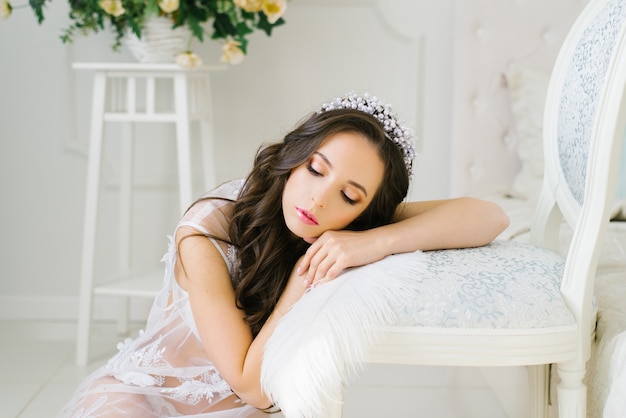 Beautiful pretty brunette bride leaned on a chair and lay down on it, closed her eyes, calm sleep.