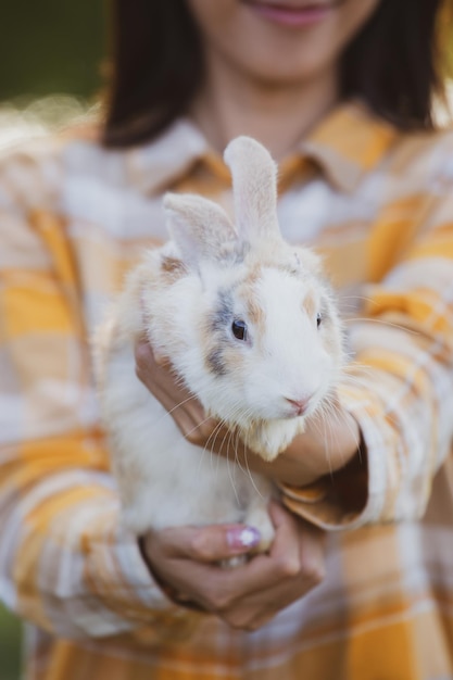 Beautiful pretty portrait of young Asian woman person with cute rabbit in pet and animal care concept happy female holding bunny at nature outdoor field with friendship easter concept