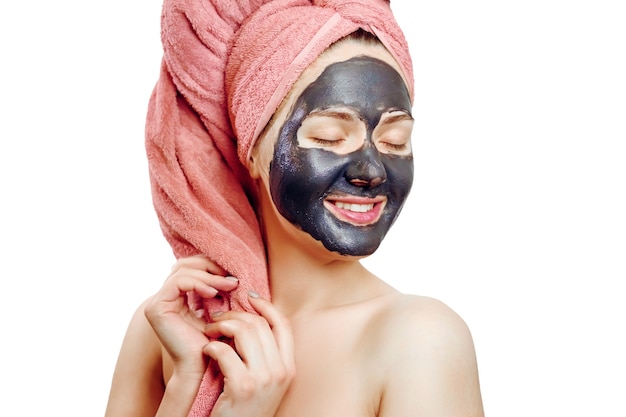 Beautiful pretty sexy girl with black face mask on the white background, close-up portrait, isolated, girl with a pink towel on her head, girl is smiling, black mask on girl's face, enjoys