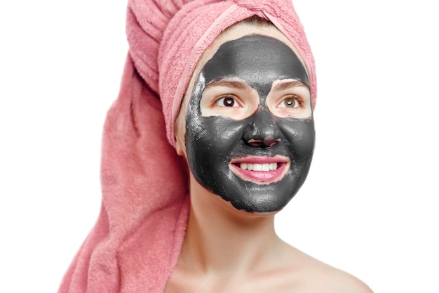 Beautiful pretty sexy girl with black face mask on the white background, close-up portrait, isolated, girl with a pink towel on her head, girl is smiling, black mask on girl's face, enjoys