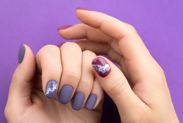 Beautiful purple burgundy matte manicure on creative background. Fashionable spring summer nail design.