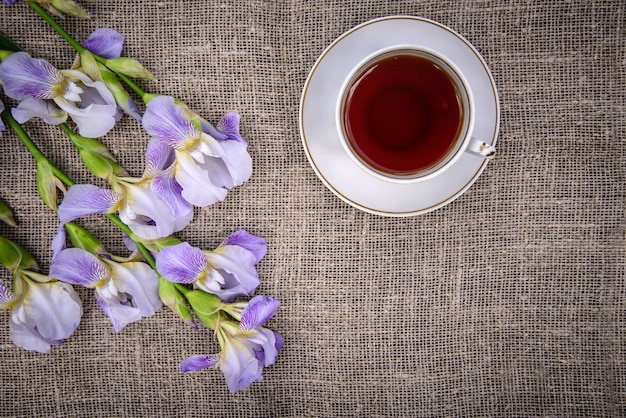 Beautiful purple flowers irises and a cup of tea on a gray canvas background