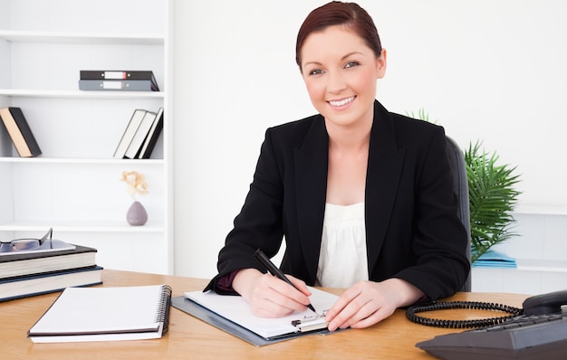 Beautiful red-haired female in suit writing on a notepad and posing