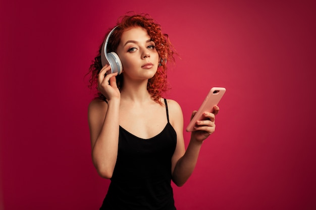 Beautiful red-haired girl in big white headphones with phone in hand listening to music 